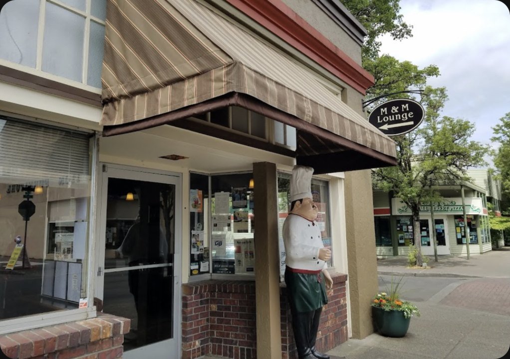 The M&M Restaurant & Lounge storefront on N Main Ave in downtown Gresham, with its striped awning and hanging M&M Lounge sign
